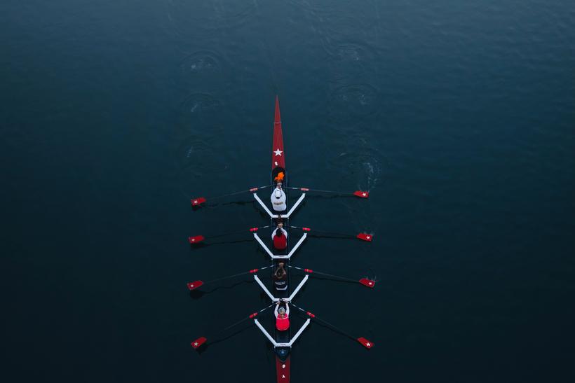 A rowing four seen from above, oars in unison on dark water