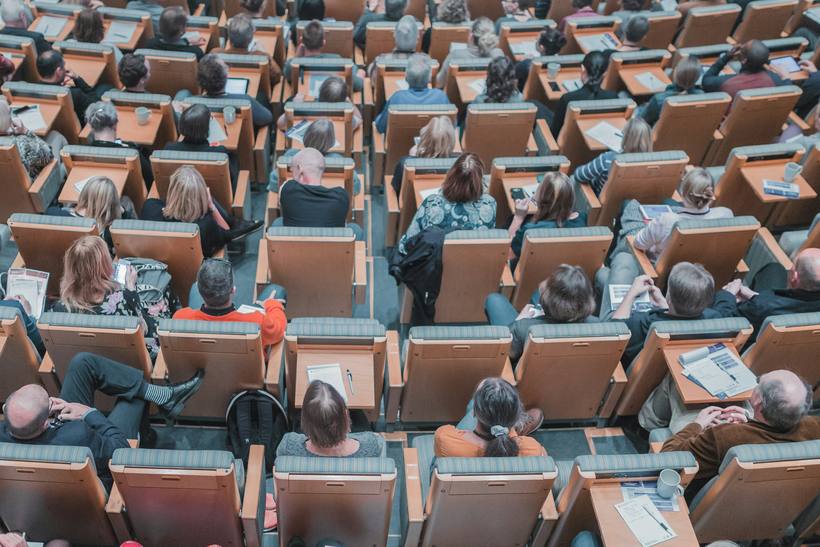 A full lecture theatre seen from above, delegates at fold-down desks