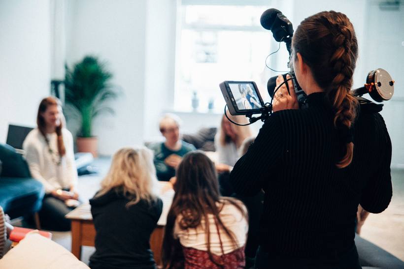 A camera operator filming a panel discussion in a bright room