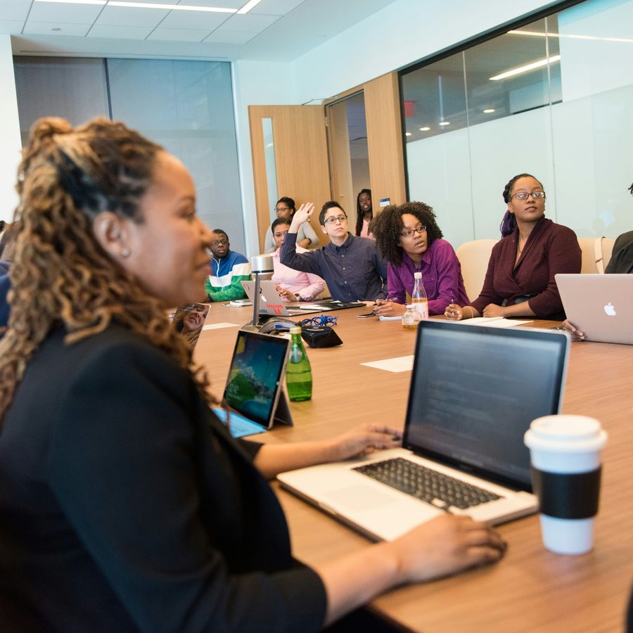 Colleagues around a conference table in a working meeting, one raising a hand to speak.