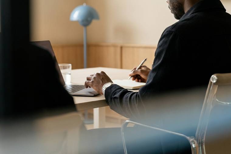 Two people working across a table, one taking notes by hand